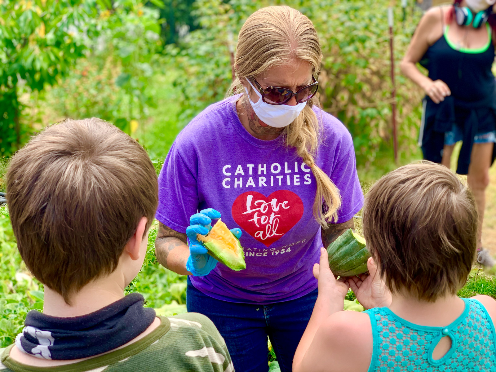 Catholic Charities worker wearing a Catholic Charities t-shirt and sharing garden-grown vegetables with kids.