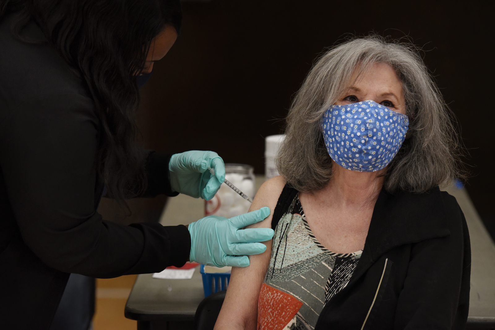 An community member wearing a floral face mask as she sits and receives a vaccination.