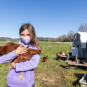 A young girl holding a chicken on a farm.