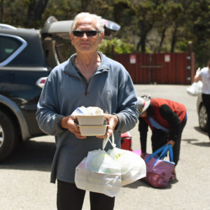 An elder community member holding trays and bags of food.