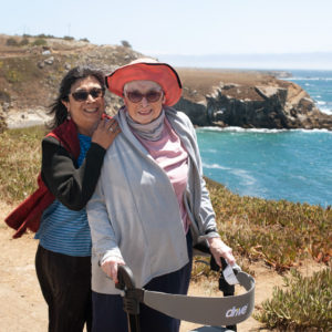 The blue ocean waves are seen behind two older ladies as they smile for a photo.