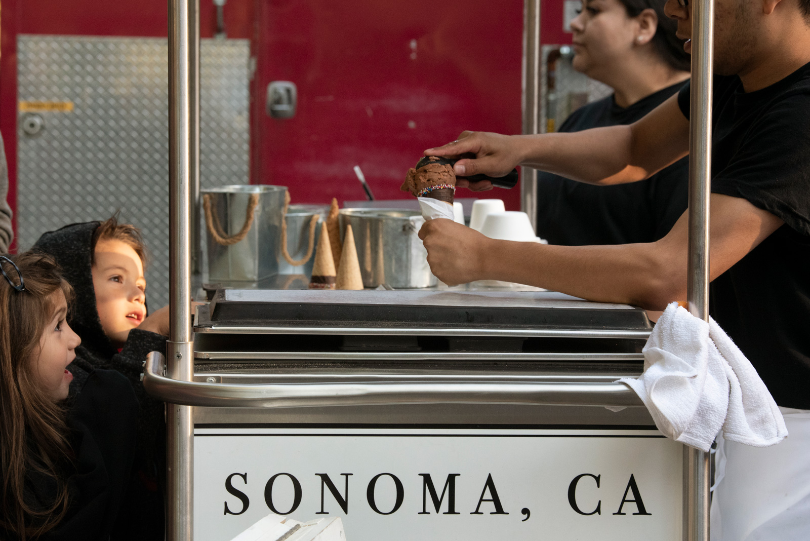 Children watching a worker scoop ice cream at a stall at the Sonoma market