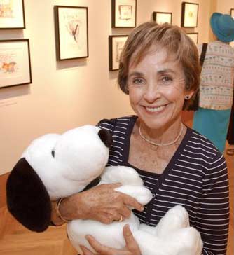 Jean Schulz smiling proudly while holding a stuffed Snoopy in her arms. 