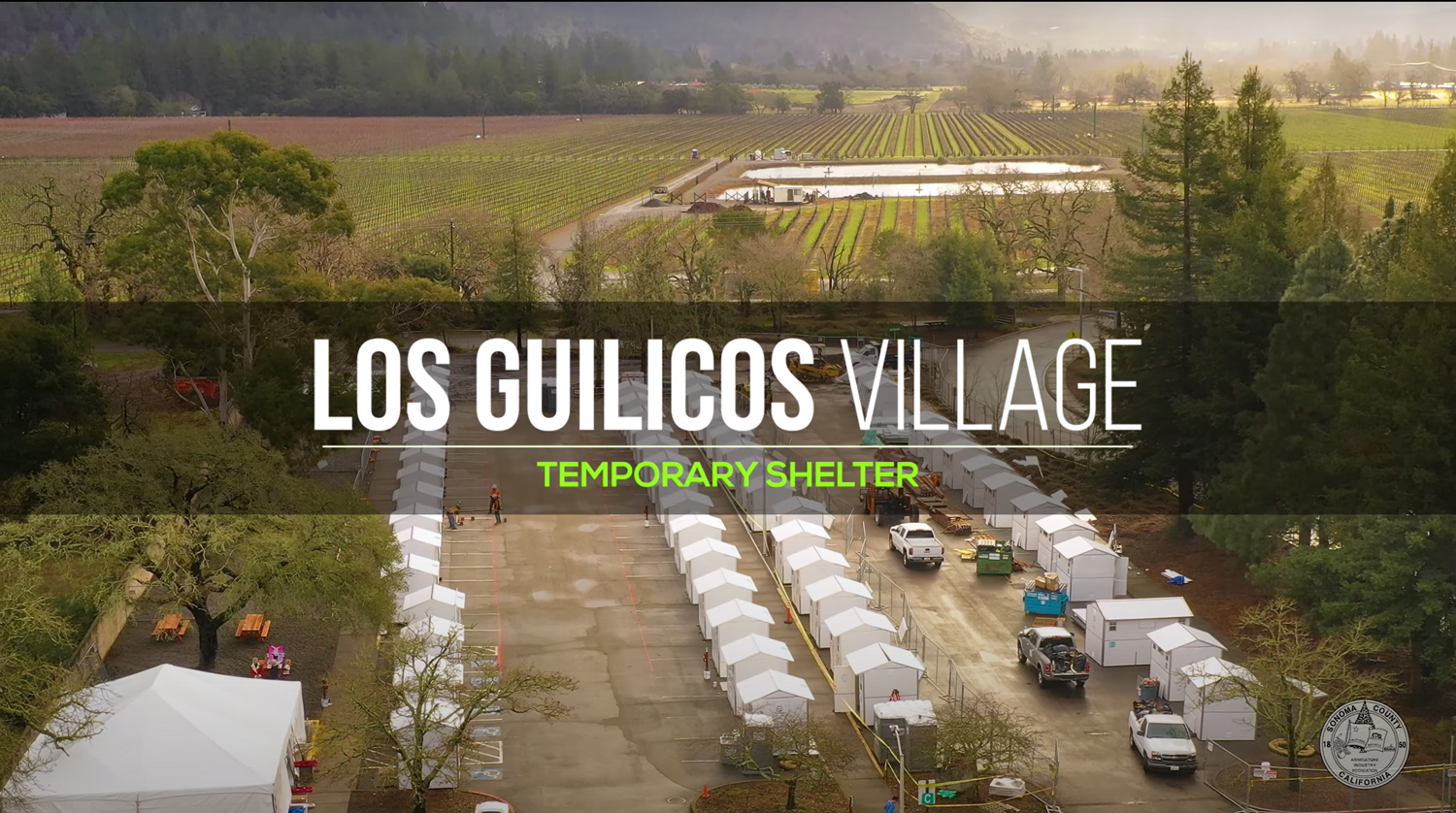 Small buildings lined up displaying the temporary shelter. Text: Los Guilicos Village, Temporary shelter