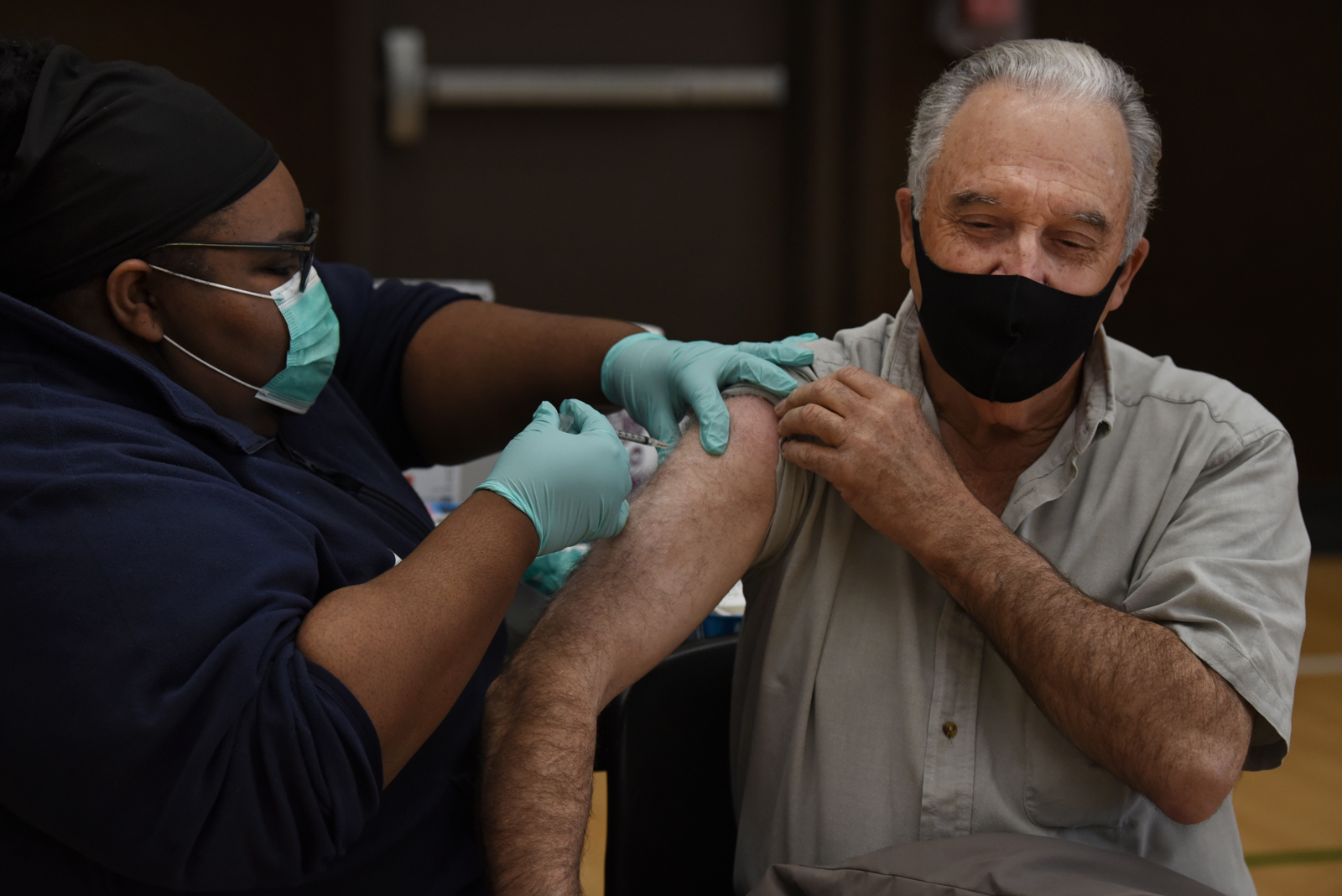 An elder community member lifts his shoulder sleeve as he receives a COVID-19 vaccine.