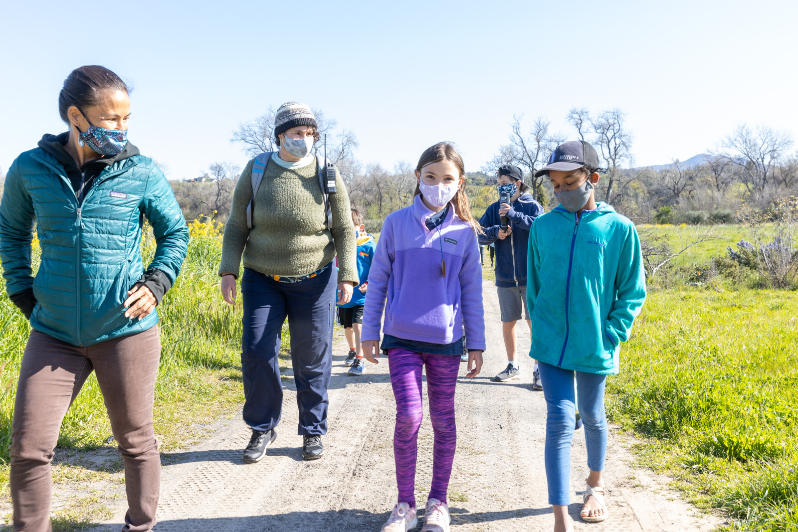 Camp goers and leaders wearing face masks and walking down a dirt road path.