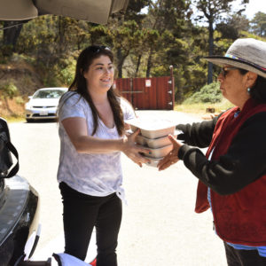 An elder community member picking up her food from a young lady holding trays of food.