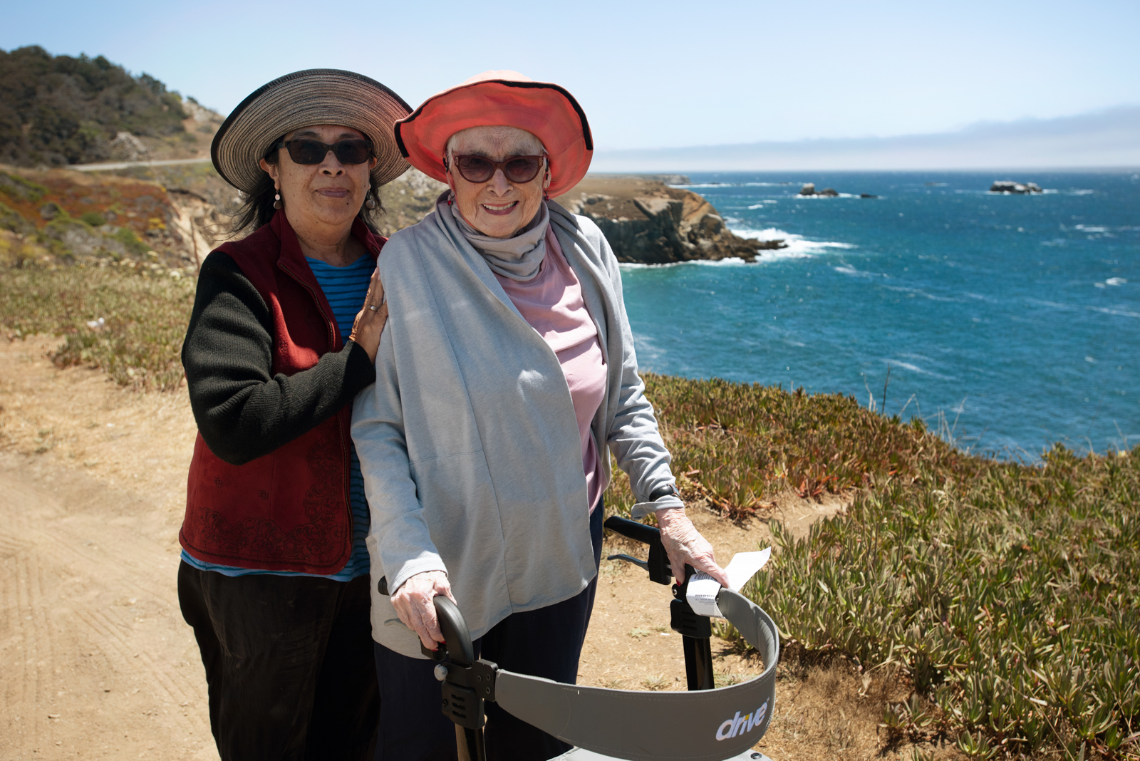 The blue ocean waves are seen behind two older ladies as they smile for a photo.