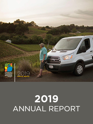 A man wearing a teal button-up and khaki shorts leaning against a white van and staring off into green hills. Text: 2019 Annual Report