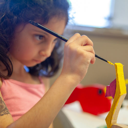 A young girl using yellow paint to paint a wooden sculpture at Art Escape in the Sonoma Valley