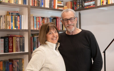 Carol Newman and Barry Sovel standing together in their home library, smiling.