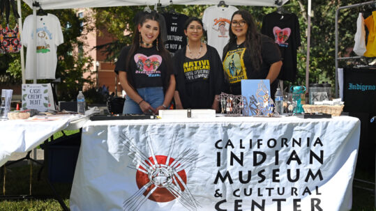 Three women standing at a California Indian Museum and Cultural Center table booth.